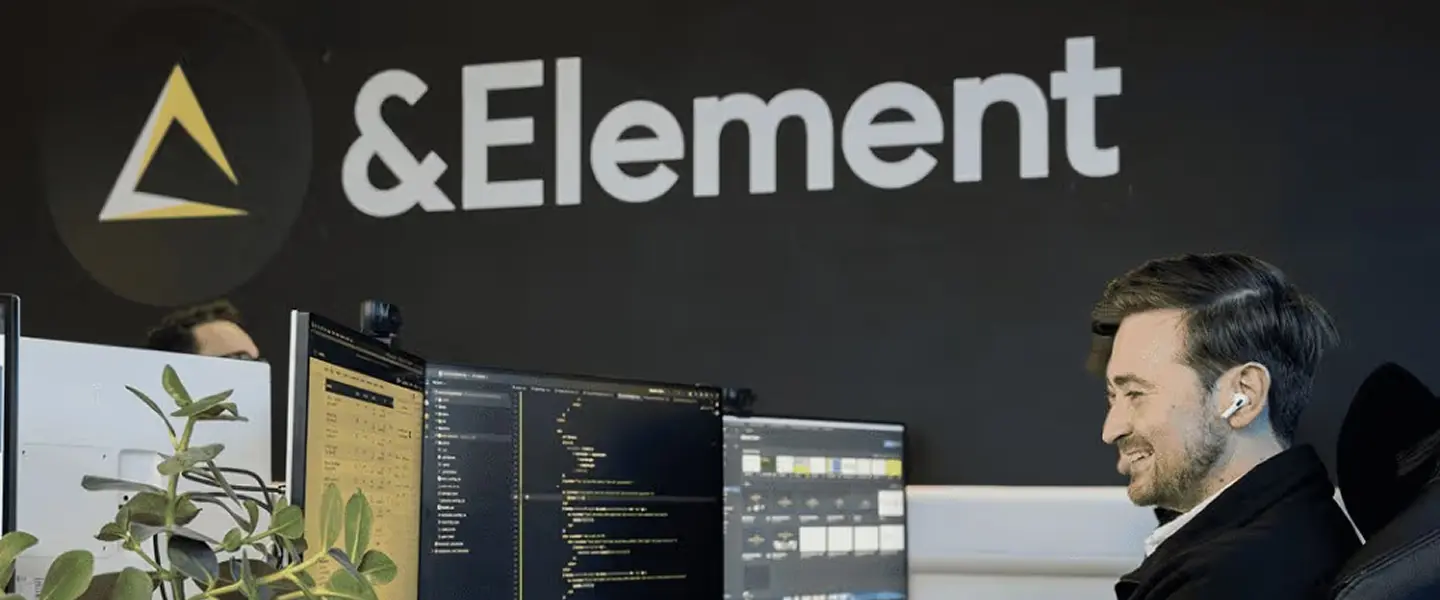 Developer working at a multi-monitor setup beneath the &Element brand wall