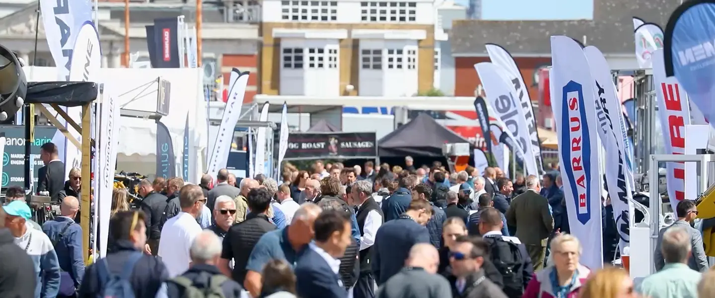 Crowded outdoor exhibition aisle with exhibitor flags at the marine show